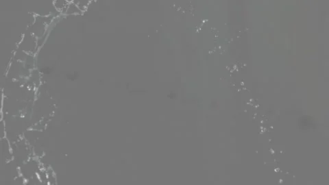 Propelled liquid sheet arcing from upper-left, thinning and breaking into drops Stock Footage 333818104