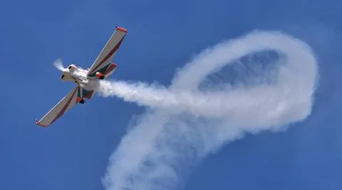 Propeller aerobatic plane draws a loop with white smoke trail in the blue sky Foto stock