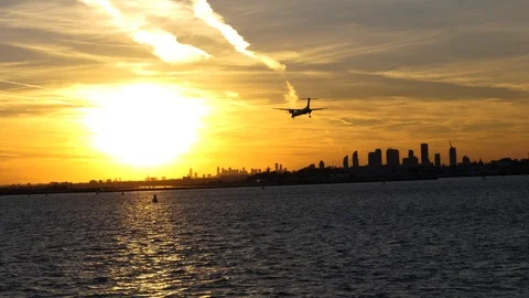 Propeller plane flying over water into sunset with skyline, airport ahead Stock Footage 90487238