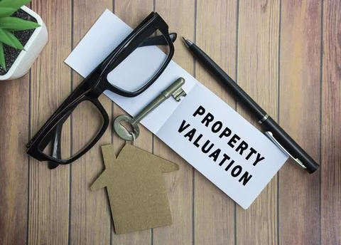 Property valuation text on notepad with house model and key on wooden desk Stock Photos