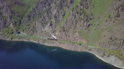 ProRes. Steam train passes through the mountains along the shore. Stock Footage 91210361