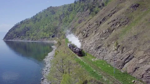 ProRes. Steam train passes through the mountains along the shore. Stock Footage 91211181