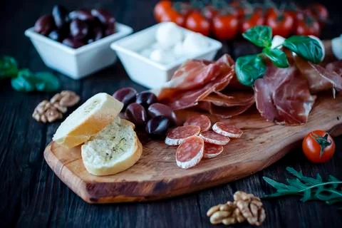 Prosciutto, bread, olives, walnut, mozzarella, salami, basil and cherry tomat Stock Photos