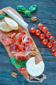 Prosciutto, bread, walnut, salami, basil and cherry tomatoes on  brown wooden Stock Photos