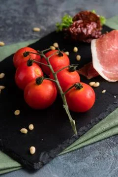 Prosciutto, cherry tomatoes and pine nuts. Fresh appetizer on the black board Stock Photos