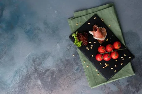 Prosciutto, cherry tomatoes and pine nuts. Fresh appetizer on the black board Stock Photos
