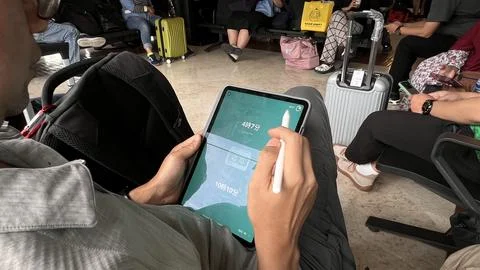 Prospective passengers wait for the plane by playing with gadgets. Stock Photos