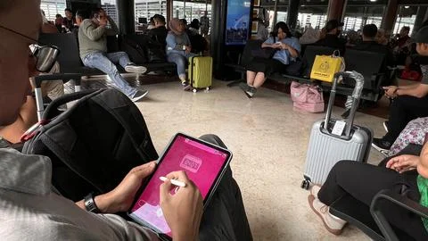 Prospective passengers wait for the plane by playing with gadgets. Stock Photos