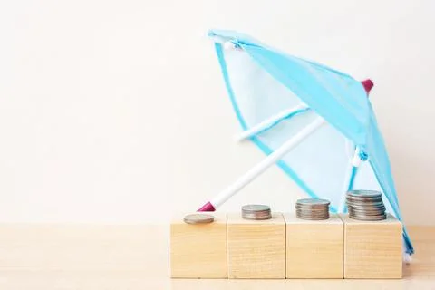 Protection on growing stack of coins money with the umbrella on biege background Stock Photos