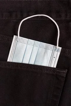 Protective face mask is lying in back pocket of black pants. Concept object. Stock Photos