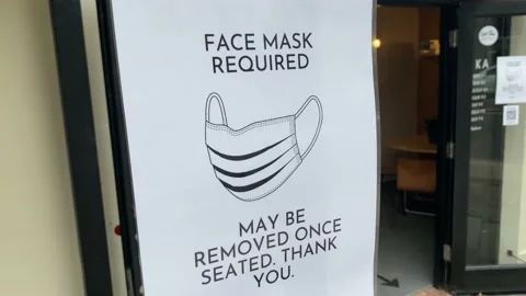 Protective face mask required sign outside a restaurant Stock Footage 137504407