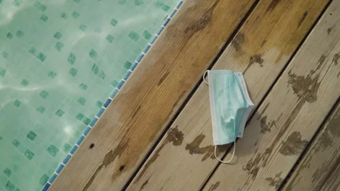 Protective face mask sitting on deck by hotel swimming pool during coronavirus Stock Footage 140768351