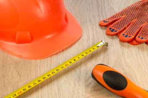 Protective helmet, gloves and tape measure on a wooden table. Stock Photos