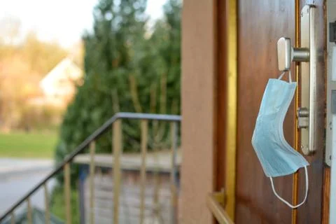 Protective mask hangs on the open front door with a view outside Foto stock