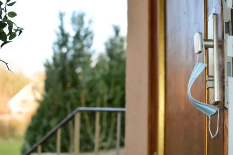 A Protective mask hangs on the open front door with a view outside Stock Photos