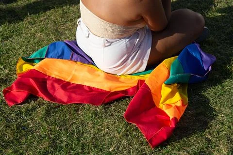 Protester sitting on a rainbow flag on the grass. Stock Photos