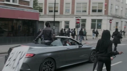Protesters marching through London Streets with Unrestrained Passengers in Car Stock Footage 132108208