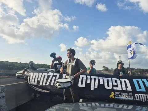 Protesters with megaphones and flags block a road under bright sky, expressing Stock Photos