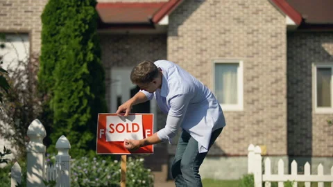 Proud man changing for sale to sold signboard in front of house, buy new home Stock Footage