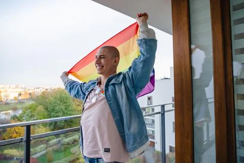 Proud non-binary queer person holding rainbow pride flag and smiling. Medium Stock Photos