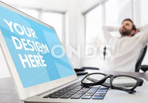 PSD template of laptop on desk and man relaxing on chair in background PSD Template