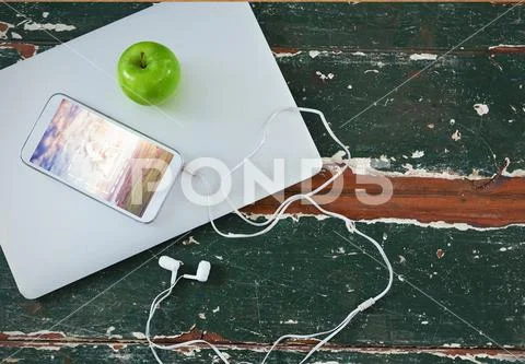 PSD template of mobile phone, laptop, green apple and headphone on wooden table PSD Template