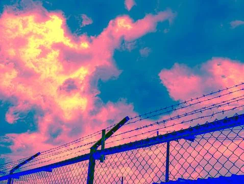 Psychedelic Barbed Wire Security Fence Against Dramatic Pink Blue Cloudy Sk.. Stock-Fotos
