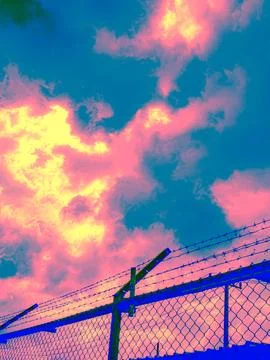 Psychedelic Barbed Wire Security Fence Against Dramatic Pink Blue Cloudy Sk.. Stock Photos