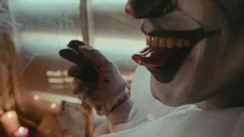 Psycho in Clown Costume Smiling while Smoking Cigarette at Creepy Place Stock Footage 250954846