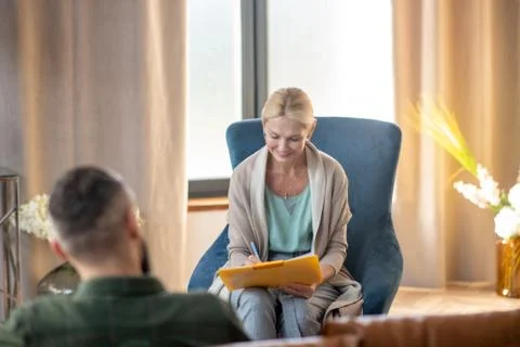 Psychoanalyst smiling while making notes and talking to patient 스톡 사진