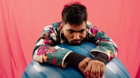 Psychologically problem man bowed on a blue exercise ball against a red bac.. Stock Footage 262485182