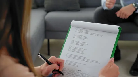 Psychologist taking notes on clipboard listens patient at psychotherapy session Video stock 163506523