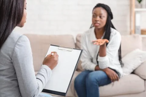 Psychologist taking notes during therapy session with her emotional female Stock Photos