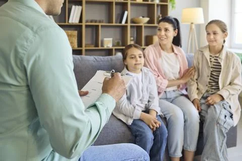Psychologist taking notes while counseling mother and daughters home session Stock Photos