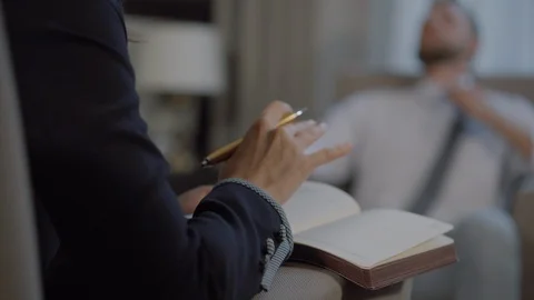 Psychologist writes in notebook and man patient is relaxing in armchair Stock Footage 119629799
