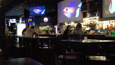 Pub Interior At Night With Some Patrons Women Drinking Big Screen Tv Playing R-L Stockbeeldmateriaal 225097415