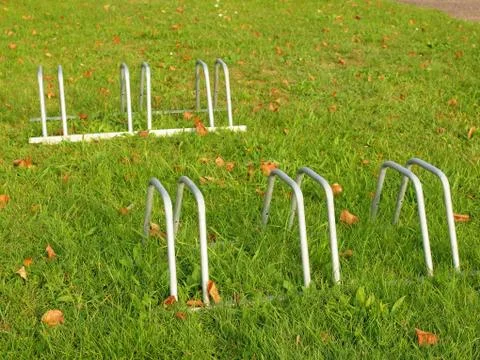 Public empty stand for bikes on grass. Gray iron frame with marks of corrosion. 库存照片