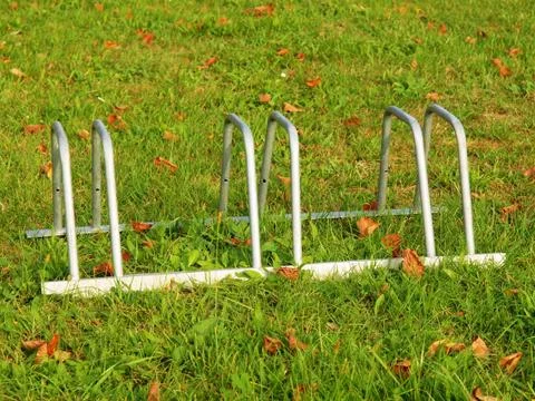 Public empty stand for bikes on grass. Gray iron frame with marks of corrosion. 库存照片