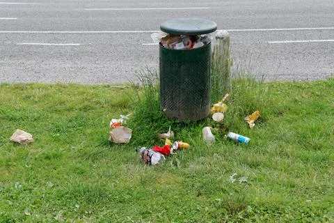 A public litter bin needs to be empty, the rubbish is falling out of it onto  Stock Photos