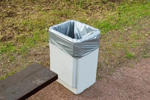 Public park trash bin with plastic liner placed next to wooden bench, Фото