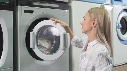 Public self-service laundry. A young pretty woman loads dirty laundry, clothes Video stock 147928233