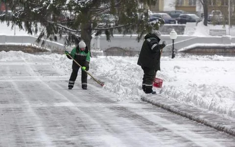 Public service workers in uniform clean the city park with shovels. Snow re.. Stock Photos