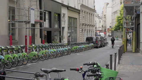 Public sharing bicycles stand parked in a long row as a cyclist rides away Stock Footage 336722099