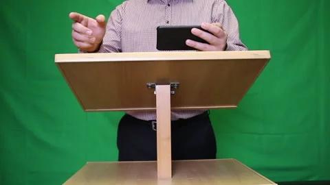 Public speaker behind the podium. In his hand holds a smartphone with speech  Stock Footage 221311077