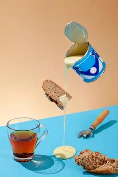 Puddle of condensed milk flows from levitating jar, can opener, black bread Stock Photos