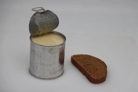 Puddle of condensed milk flows from levitating jar, can opener, black bread Foto stock