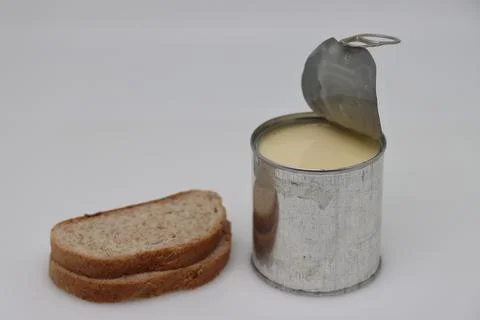 Puddle of condensed milk flows from levitating jar, can opener, black bread Foto stock