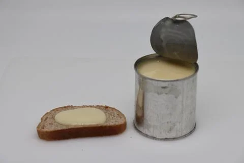 Puddle of condensed milk flows from levitating jar, can opener, black bread Foto stock