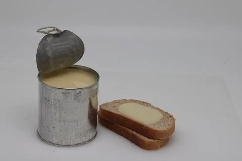 Puddle of condensed milk flows from levitating jar, can opener, black bread Foto stock