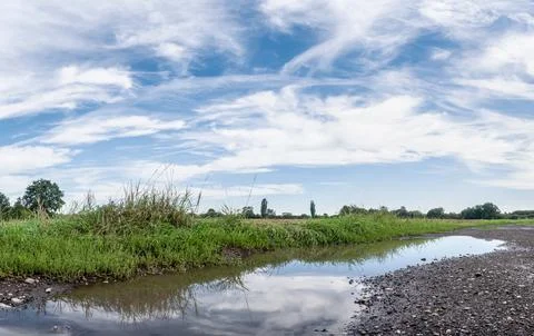Puddle on dirt road in middle of meadows and fields Фото